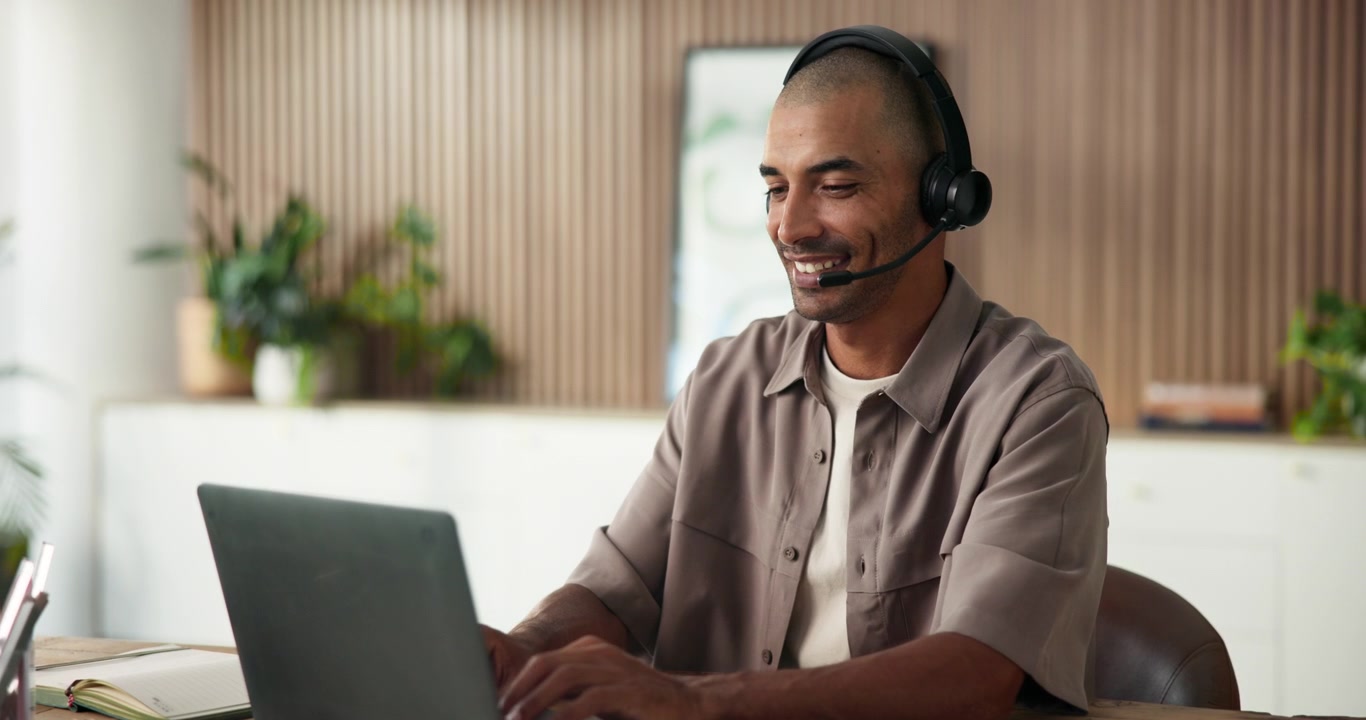 Man Wearing Headset Working on Laptop in Home Office