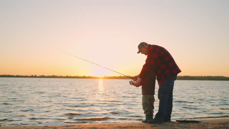 El-Anciano-Está-Echando-Caña-En-El-Agua-Del-Río.-Su-Nieto-Está-Viendo-La-Naturaleza-En-La-Orilla.