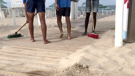 in the tranquil morning, a diligent man clears sand using broom from the seawall, restoring the beach's allure after a vibrant day of visitors