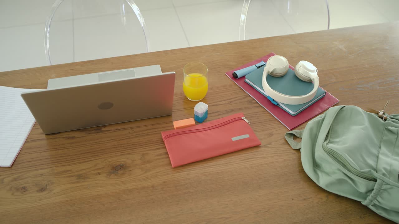 Camera is shifting right and moving closer revealing laptop orange juice coral pouch on wood table
