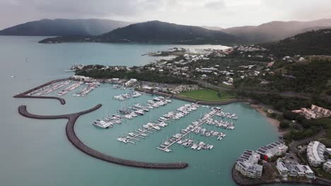 Port-Airlie-Beach-Bay-Lagoon-Coral-Sea-marina-aerial-drone-rain-clouds-mist-sunrise-morning-heart-of-Great-Barrier-Reef-Whitsundays-Whitehaven-jetty-yachts-sailboats-buildings-forward-reveal-motion