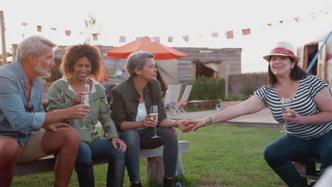 group of mature friends sitting around fire and drinking at outdoor campsite bar