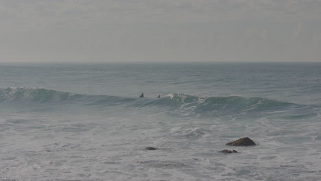 Three-Surfers-wait-in-the-water-for-a-wave-to-come,-then-one-finds-one-in-Manly-Beach-Australia