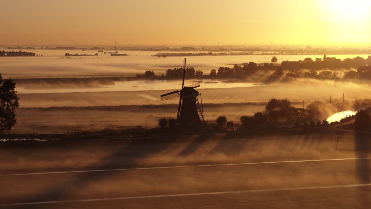 Early morning fog rising near silhouette of old windmill with bright yellow sunshine
