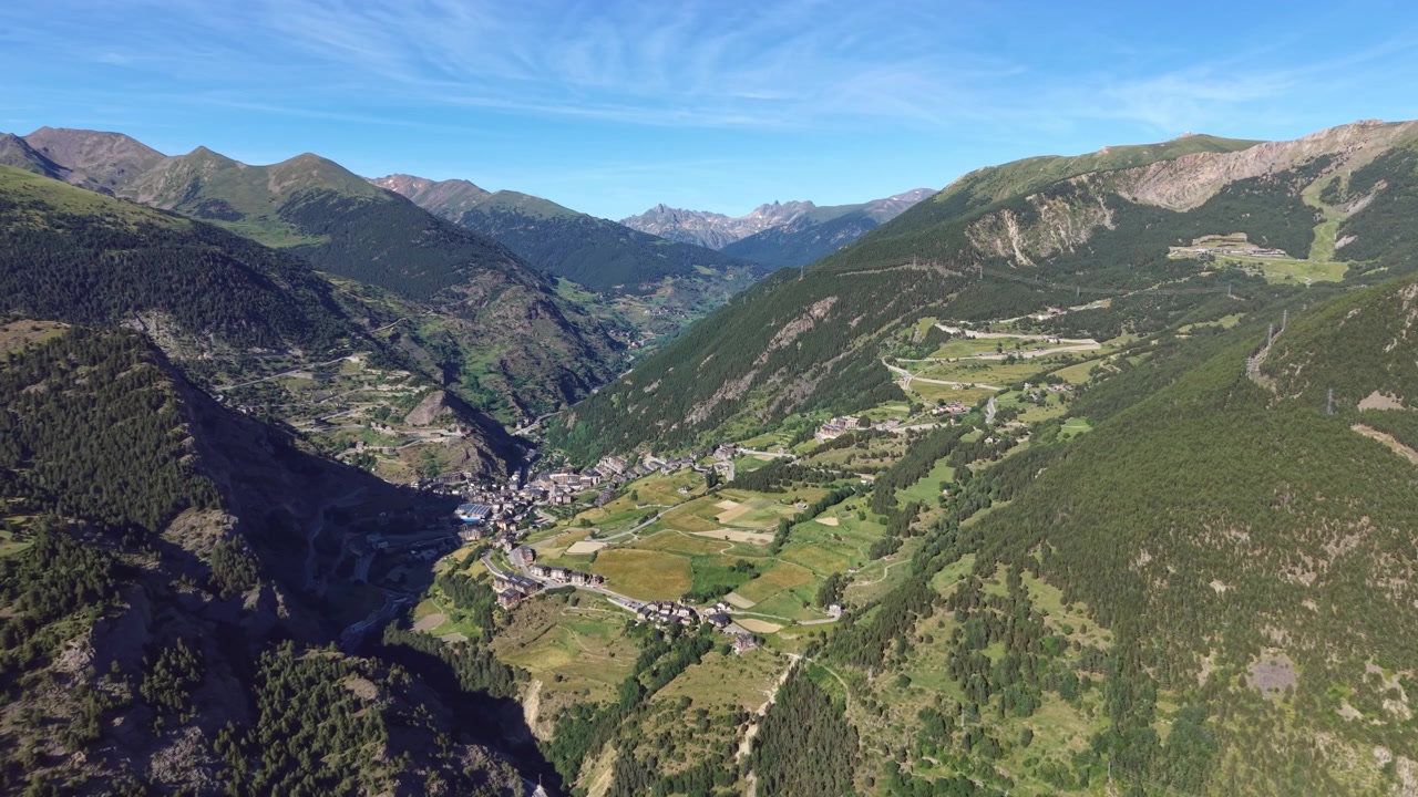 Andorra'da yemyeşil bir dağ vadisine kurulmuş Canillo köyü, ormanlık yamaçları, tarım alanları, kıvrımlı yolları ve mavi gökyüzü altındaki Pireneler'in zirveleriyle.