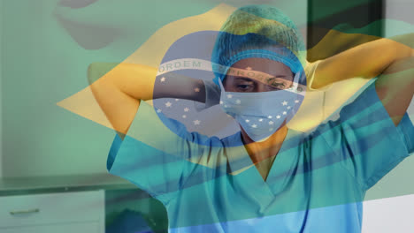 Animation-of-waving-brazil-flag-against-biracial-female-surgeon-wearing-surgical-mask-at-hospital