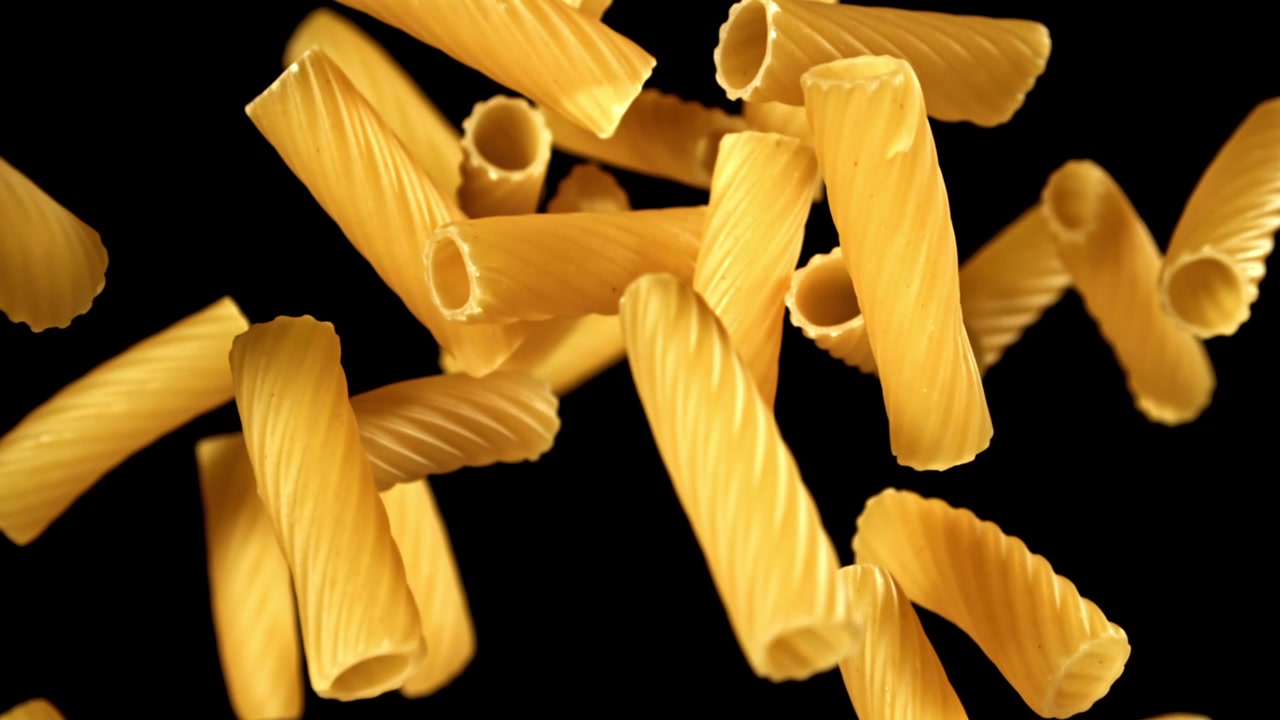 Rigatoni secchi che cadono al rallentatore su sfondo nero
