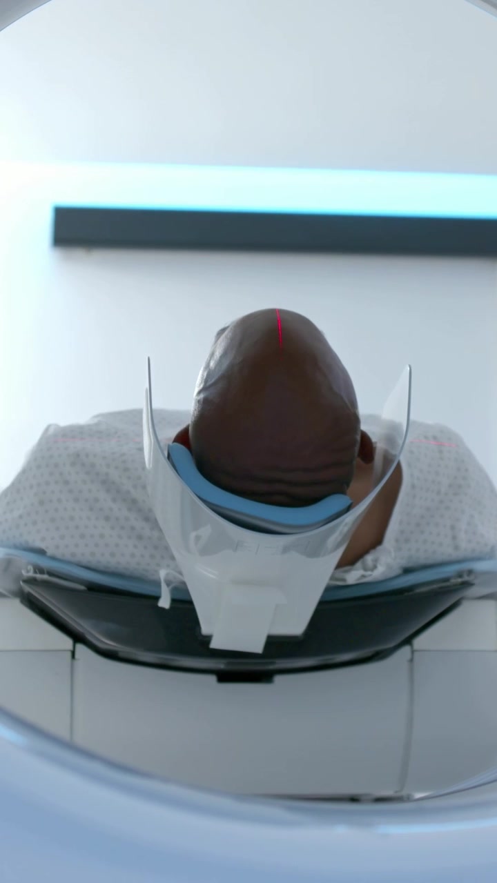 Video verticale: Telecamera che si allontana da un'apertura, mostrando un uomo supino con camice da clinica e poggiatesta, con un laser rosso.