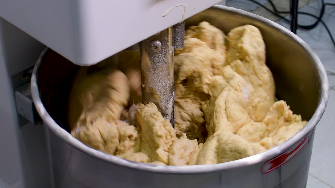 Statisk nærbillede af professionelle hænder, der ælter smør ind i en fyldig, gul dej til håndværksmæssig Pan de Jamon-produktion