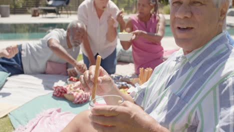 Smiling-diverse-senior-man-and-friends-having-picnic-in-sunny-garden,-unaltered,-in-slow-motion