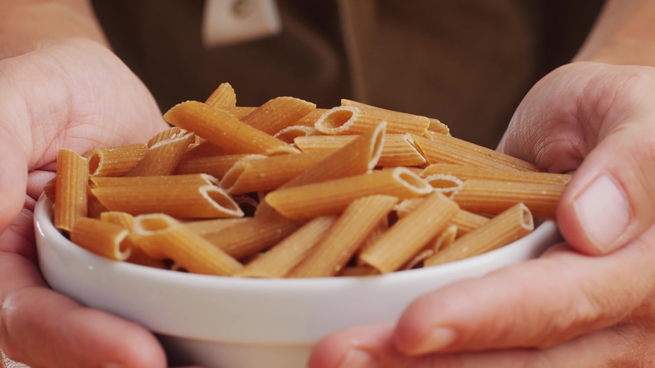 Pasta integrale biologica, maccheroni di semola di grano duro, penne rigate crude in una ciotola di legno. Filmato 4k di alta qualità