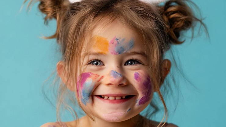 Un bambino vivace che sorride gioiosamente con il viso dipinto di colori vivaci su uno sfondo blu brillante, catturando l'essenza della giocosità e della creatività in un ambiente divertente.