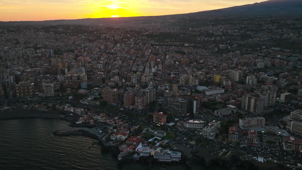 Città costiera metropolitana di Catania al tramonto ai piedi dell'Etna in Sicilia, Italia. Ripresa aerea con tilt-up.