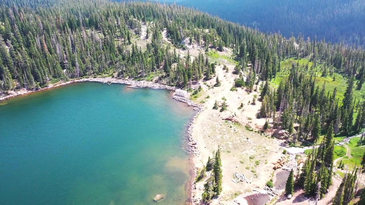 Drone Aereo che Sorvola Uomo e Donna Seduti, che si Abbracciano e si Baciano a Nederland, Colorado, vicino a un Lago Azzurro e Limpido e una Foresta di Pini durante l'Estate nelle Montagne Rocciose.
