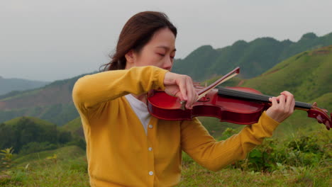 Primer-Plano-En-Cámara-Lenta-De-Una-Mujer-De-Pelo-Castaño-Tocando-El-Violín-En-La-Naturaleza-Con-Vistas-A-La-Montaña