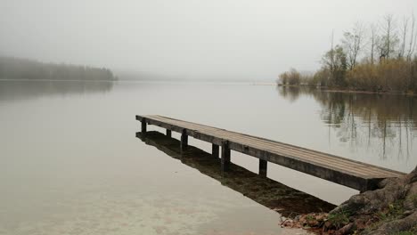 a pier leading out to a lake on a moody and minimalist day at lake bohinj