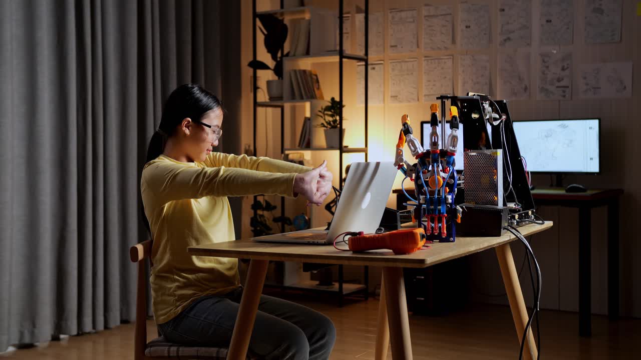 십대 아시아 소녀가 집에서 노트북에서 사이보그 손에 대해 일하는 동안 스트레칭