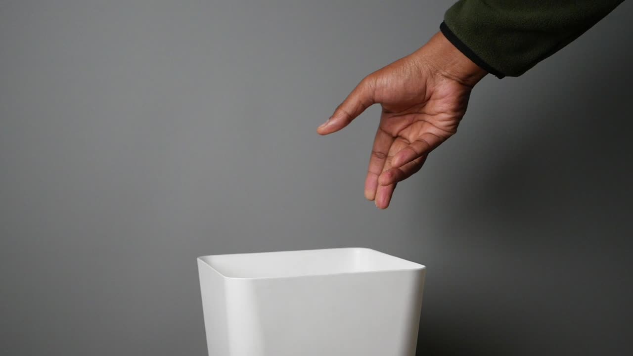 Hand disposing of trash into a white trash can