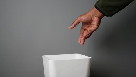 hand disposing of trash into a white trash can