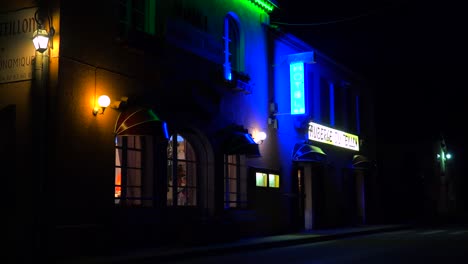 a small french hotel at night with neon sign flashing