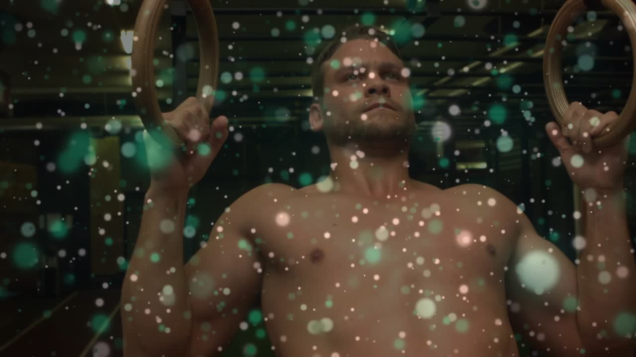 Man grasping wood rings, pulling, holding torso for fitness while green bokeh drifting across lens