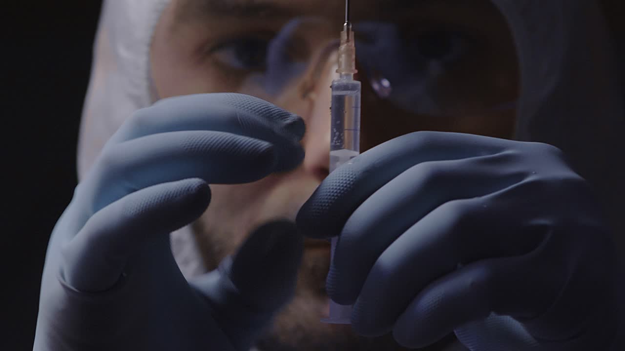 médico en traje protector con jeringa, primer plano de la cara, fondo oscuro