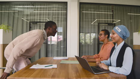 young man sits at the office table and shakes hand to two businesswomen