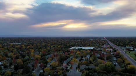 Toma-Aérea-De-Un-Dron-Empujando-Hacia-Una-Hermosa-Puesta-De-Sol-Nublada-Sobre-Un-Barrio-Residencial-Denso-De-árboles