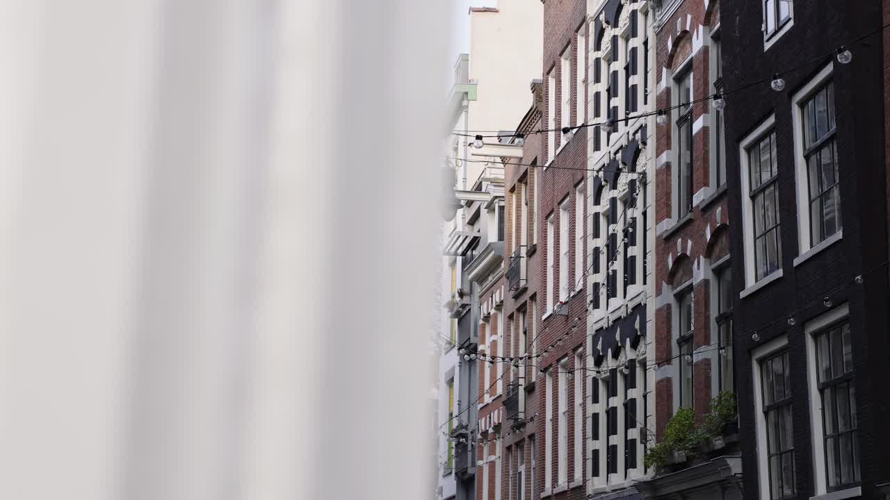 네덜란드 암스테르담 의 한 거리 에 있는 아파트 건물 들 사이 에 매달려 있는 야외 전구 들