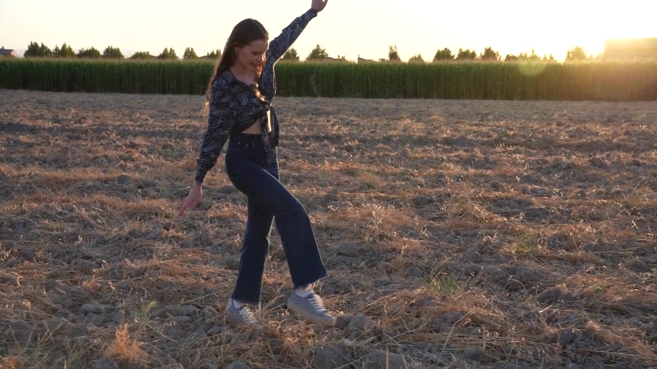 Uma bela silhueta de uma dançarina posando graciosamente num campo iluminado pelo sol ao pôr do sol.