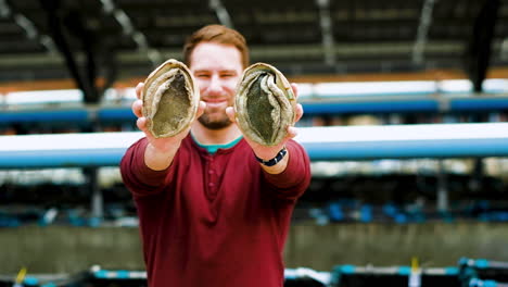 smiling caucasian man holds up two big south african abalones, aquafarming