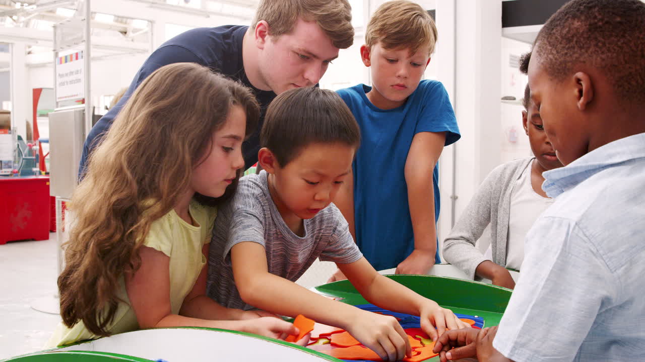 un maestro ayudando a los niños de la escuela a hacer un rompecabezas de ciencias