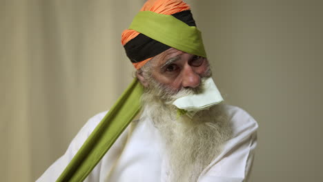 Fotografía-De-Estudio-De-Un-Hombre-Sikh-Mayor-Con-Barba-Atando-Una-Tela-Para-Un-Turbante-Contra-Un-Fondo-Liso,-Tomada-En-Tiempo-Real-1