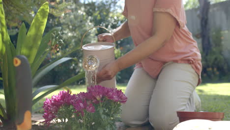 Mujer-Birracial-Mayor-Regando-Flores-En-Un-Jardín-Soleado-En-Casa,-Cámara-Lenta