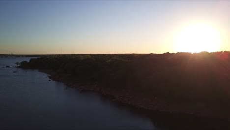 Toma-Aérea-Durante-La-Puesta-De-Sol-De-La-Orilla-Del-Lago-Y-El-Denso-Bosque