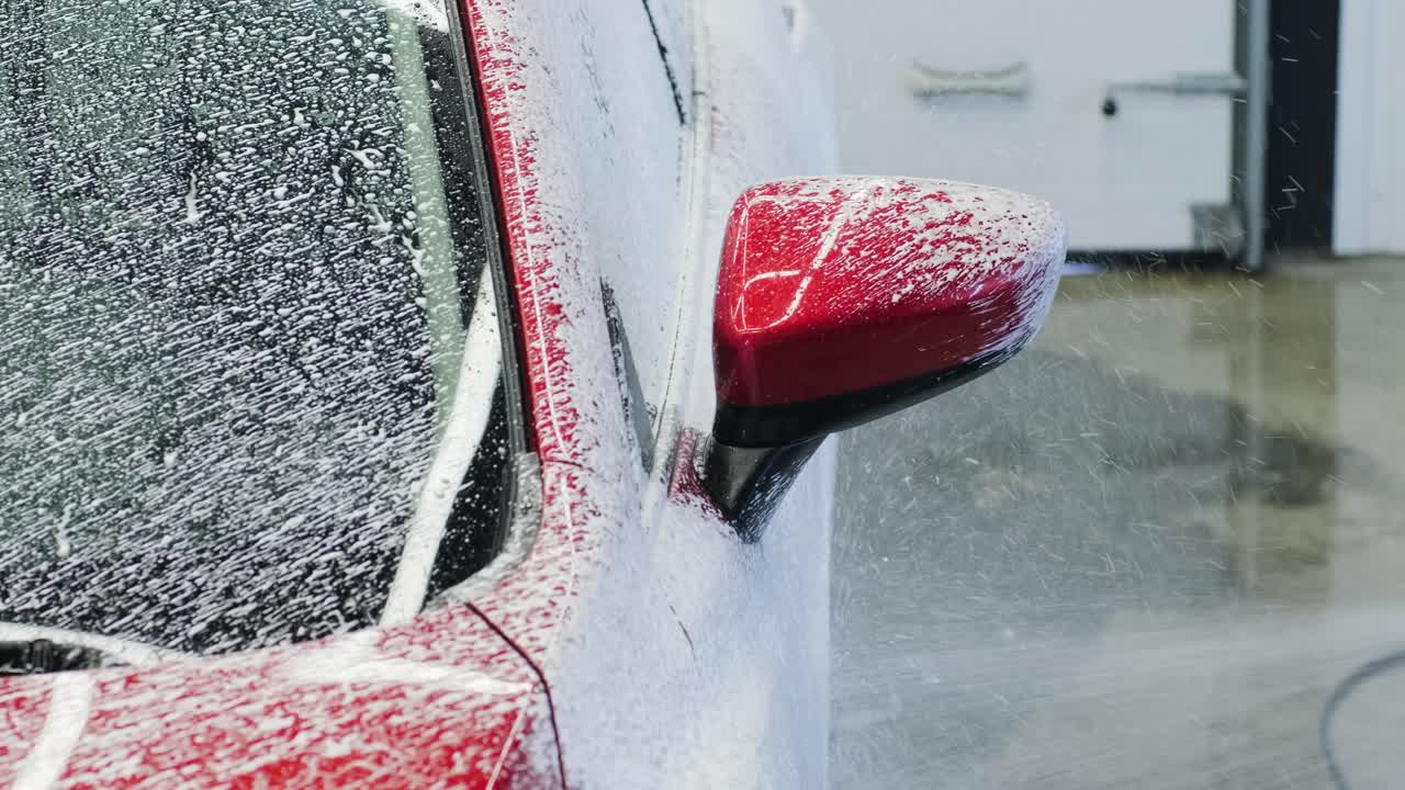 Lavaggio auto con schiuma e acqua ad alta pressione. Auto rossa.