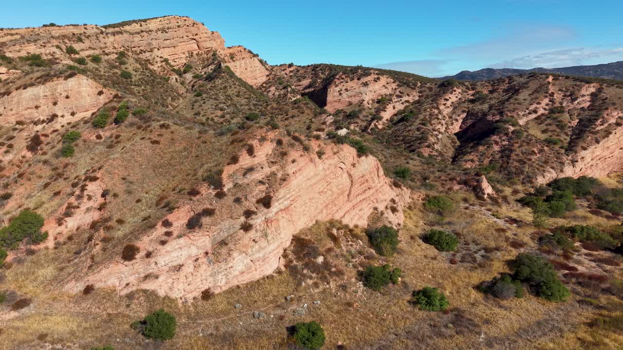 Sweeping aerial view over the arid ridges and rocky terrain of Black Star Canyon, California. Rugged hills and stratified cliffs dominate the wilderness landscape under clear blue skies