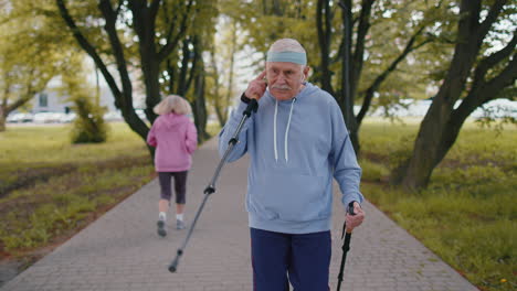 senior healthy retired man grandfather training nordic walking use ski trekking poles in summer park