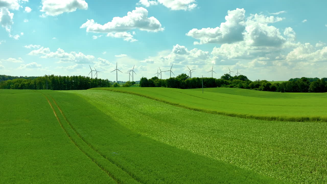 Aerial view of green fields with wind turbines and a clear blue sky with scattered clouds
