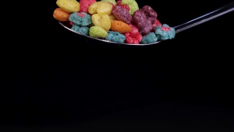 vibrant cereal pieces drop from a spoon against a black background, captured in slow motion with dramatic lighting