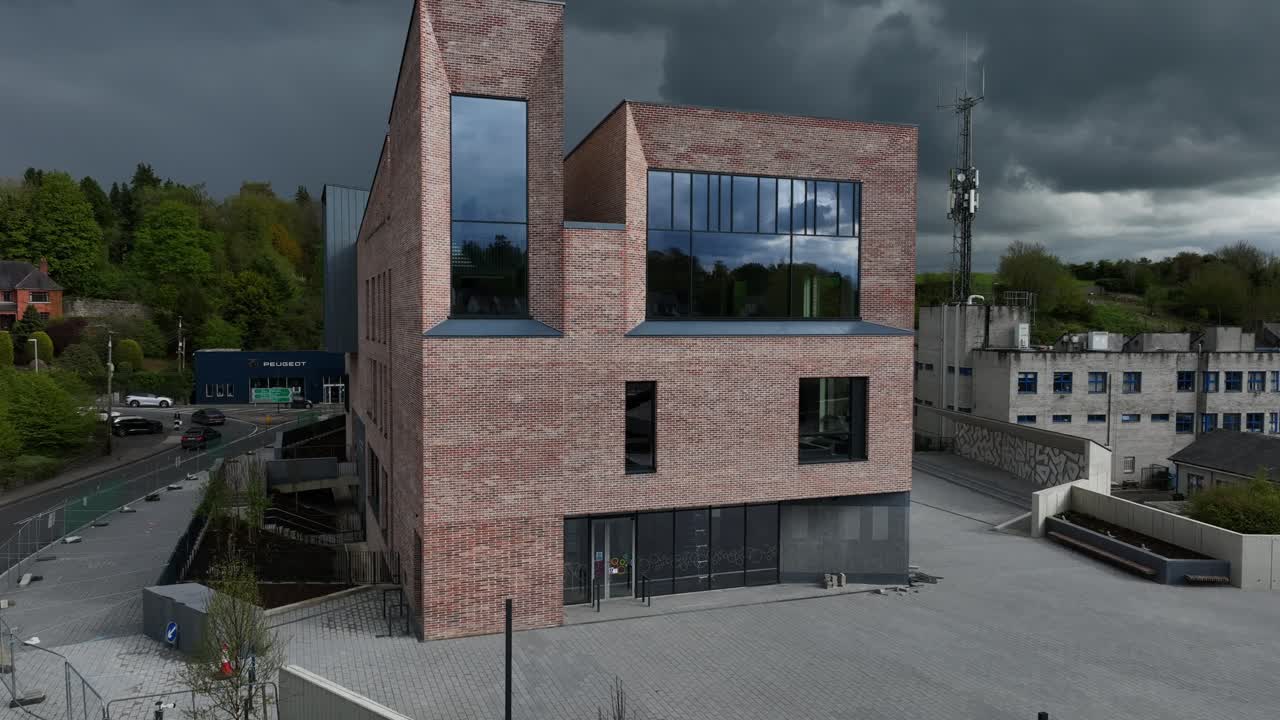 Peace Campus, County Monaghan, Ireland, April 2024. Drone hovers infront of the facade of the Monaghan County Museum building against a backdrop of dark moody clouds.