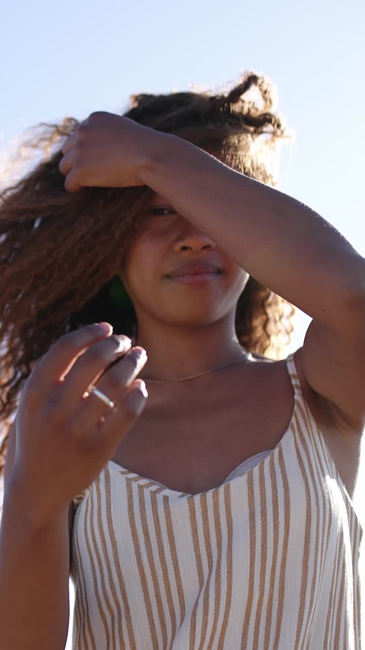 Giovane donna con capelli ricci bagnata dalla luce del sole all'aperto