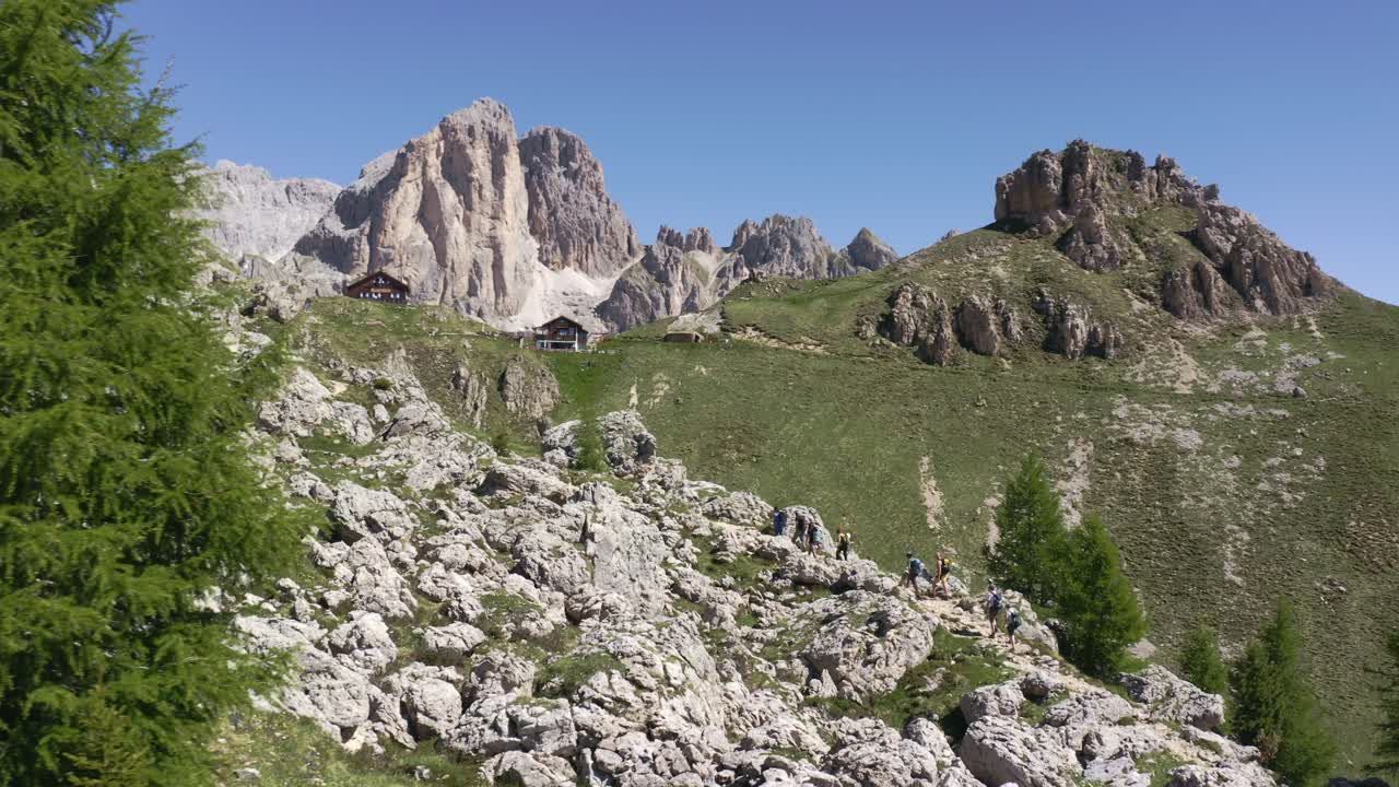 toma de seguimiento aéreo que muestra a un grupo de excursionistas en la ruta de senderismo rifugio roda di vael durante el día soleado en dolomitas