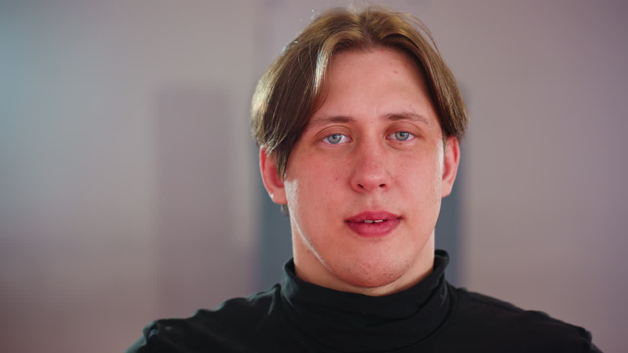 Chap in black turtleneck stares into camera with calm expression under bright indoor lights, capturing mood of confidence, presence, discipline, strength, and determination in controlled environment with focus