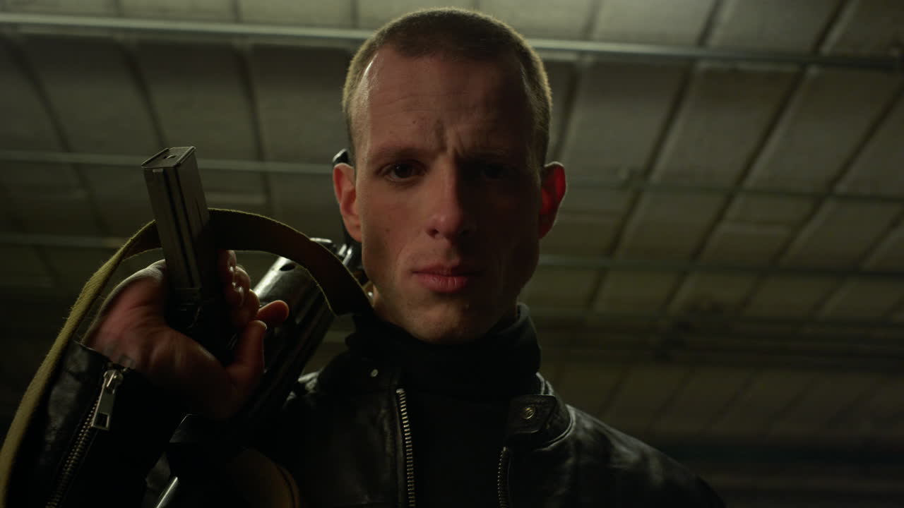 Criminal posing at camera with assault rifle. Male robber holding modern weapon