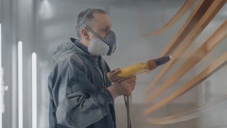 un hombre con un traje de protección y una máscara pintor rocía pintura en las partes. pequeña tienda de pintura de negocios. taller para pintar partes.