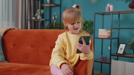 Girl-kid-enjoying-conversation-on-mobile-phone-with-friend-relaxing-sitting-on-sofa-at-home-alone