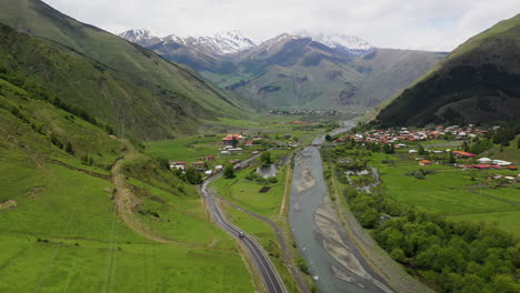 wide drone shot of a road in the caucasus mountains with juta georgia in the distance