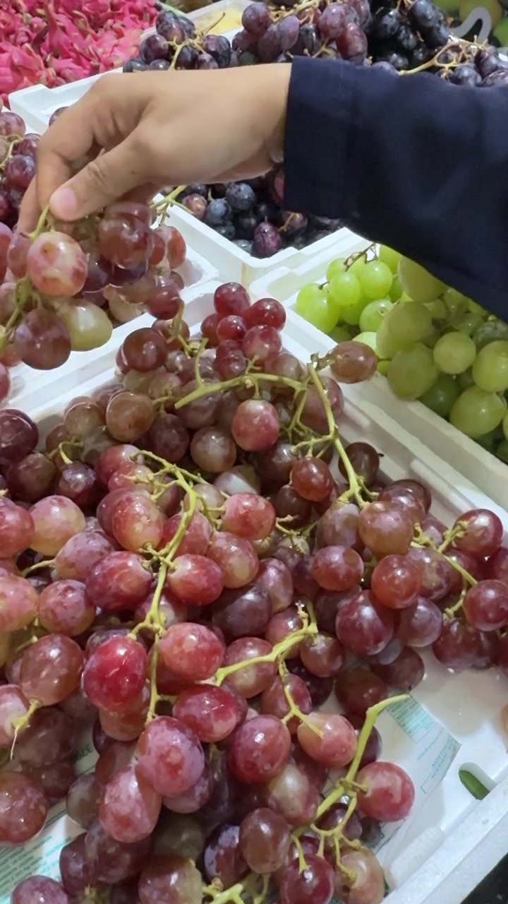 Mão de uma pessoa selecionando uvas vermelhas em uma banca de mercado