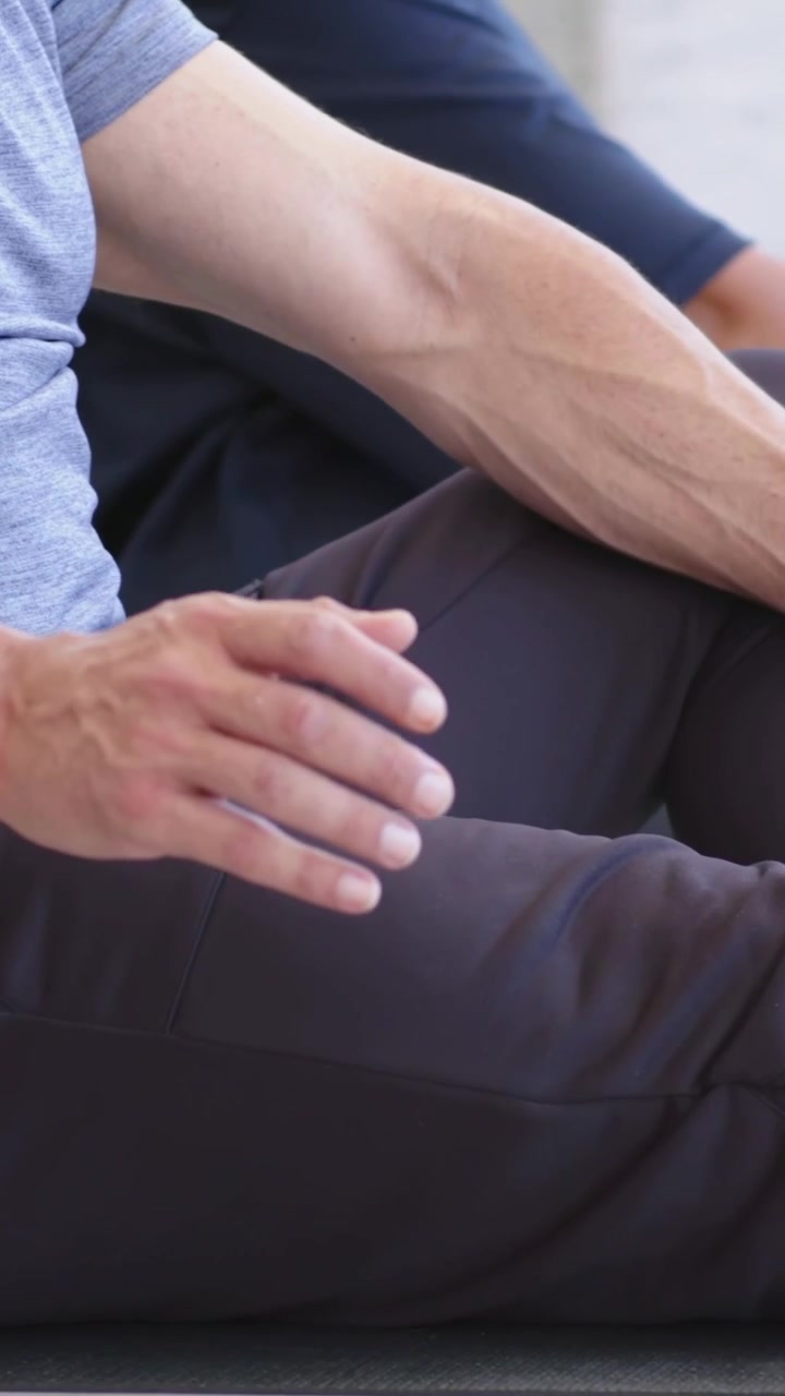 Vertical video: Panning showing couple doing breathwork on home mats, man shifting legs in grey tee